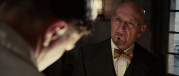 Movie still from “Shutter Island” (2010), directed by Martin Scorsese – An older man wearing a suit and a bow tie; Close Up shot, Over the shoulder angle
