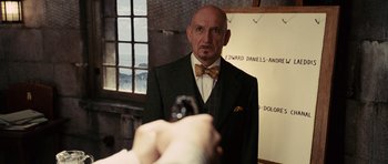 Movie still from “Shutter Island” (2010), directed by Martin Scorsese – A man in a suit and bow tie holding a gun; Close Up shot, Over the shoulder angle