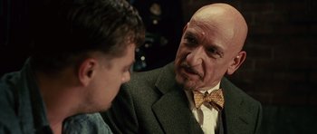 Movie still from “Shutter Island” (2010), directed by Martin Scorsese – A man wearing a suit and bow tie talking to another man in a suit; Close Up shot, Over the shoulder angle
