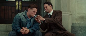 Movie still from “Shutter Island” (2010), directed by Martin Scorsese – Two men in suits and ties are smoking a cigarette together; Medium shot, Low angle