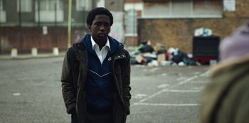 Movie still from “Top Boy” (2011), created by Ronan Bennett – A man standing in the middle of the street; Medium shot, Over the shoulder angle