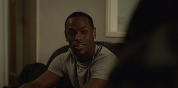 Movie still from “Top Boy” (2011), created by Ronan Bennett – A man sitting on a couch wearing a gray t - shirt; Close Up shot, Over the shoulder angle