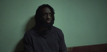 Movie still from “Top Boy” (2011), created by Ronan Bennett – A man with long hair and a dreadlock is looking at the camera; Close Up shot, Low angle