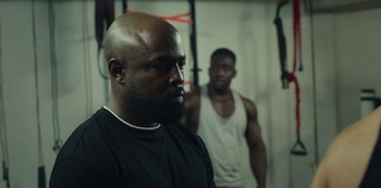 Movie still from “Top Boy” (2011), created by Ronan Bennett – A man with a beard is standing next to another man in a gym; Close Up shot, Over the shoulder angle