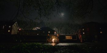 Movie still from “Top Boy” (2011), created by Ronan Bennett – Two people sitting on a bench in front of a fire pit at night; Extreme Wide shot, High angle