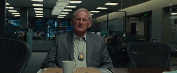 Movie still from “Sicario” (2015), directed by Denis Villeneuve – An older man sitting at a table with a cup of coffee in front of him; Medium shot, Over the shoulder angle