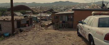 Movie still from “Sicario” (2015), directed by Denis Villeneuve – A dirt field with a house and some buildings; Extreme Wide shot, Over the shoulder angle