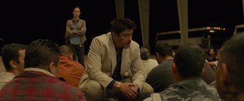 Movie still from “Sicario” (2015), directed by Denis Villeneuve – A man sitting on the ground in front of a group of people; Medium shot, Over the shoulder angle