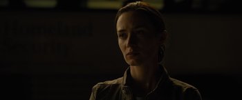 Movie still from “Sicario” (2015), directed by Denis Villeneuve – A woman in a brown shirt is in a dark room; Close Up shot, Low angle