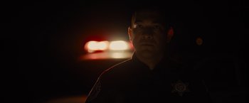 Movie still from “Sicario” (2015), directed by Denis Villeneuve – A man in a police uniform in the dark with lights in the background; Close Up shot, Low angle