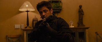 Movie still from “Sicario” (2015), directed by Denis Villeneuve – A man in black jacket holding a gun in a room; Medium shot, Over the shoulder angle