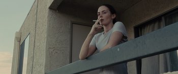 Movie still from “Sicario” (2015), directed by Denis Villeneuve – A woman smoking a cigarette while leaning on a balcony railing; Medium shot, Low angle
