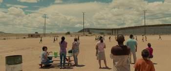 Movie still from “Sicario” (2015), directed by Denis Villeneuve – A group of people standing on top of a dirt field; Extreme Wide shot, Over the shoulder angle