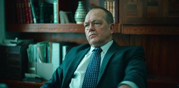 Movie still from “Top Boy” (2011), created by Ronan Bennett – An older man wearing a suit and tie sitting in front of a book shelf; Close Up shot, Low angle