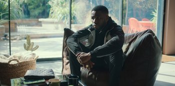 Movie still from “Top Boy” (2011), created by Ronan Bennett – A man sitting on a leather chair next to a window; Medium shot, Over the shoulder angle