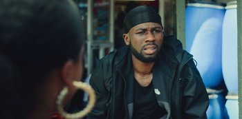 Movie still from “Top Boy” (2011), created by Ronan Bennett – A man in a black hat and a black jacket is talking to a woman; Close Up shot, Over the shoulder angle