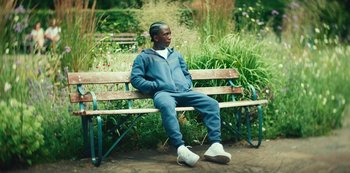 Movie still from “Top Boy” (2011), created by Ronan Bennett – A man sitting on top of a wooden park bench; Medium shot, High angle