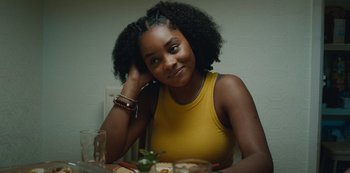 Movie still from “Top Boy” (2011), created by Ronan Bennett – A woman sitting at a table with a plate in front of her; Close Up shot, Over the shoulder angle