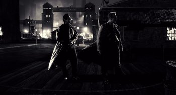 Movie still from “Sin City” (2005), directed by Frank Miller – A couple of men walking down a street at night; Wide shot, Low angle