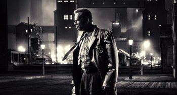 Movie still from “Sin City” (2005), directed by Frank Miller – A black and white photo of a man in a suit and tie; Medium shot, Low angle