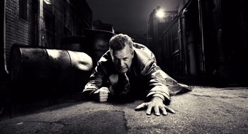 Movie still from “Sin City” (2005), directed by Frank Miller – A black and white photo of a man laying on the ground; Wide shot, Low angle