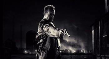 Movie still from “Sin City” (2005), directed by Frank Miller – A man holding a gun while standing in front of a city; Medium shot, Low angle