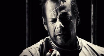 Movie still from “Sin City” (2005), directed by Frank Miller – A black and white photo of a man holding a cigarette; Close Up shot, Overhead angle