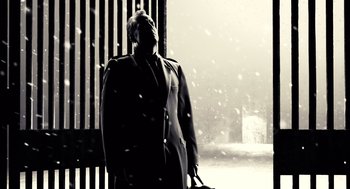 Movie still from “Sin City” (2005), directed by Frank Miller – A man standing in the snow holding a bag; Medium shot, Low angle