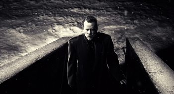 Movie still from “Sin City” (2005), directed by Frank Miller – A black and white photo of a man in a trench coat; Medium shot, Low angle