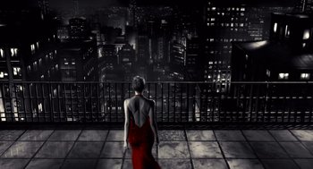 A woman in a red dress looking out over a city at night