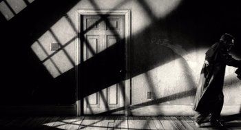 Movie still from “Sin City” (2005), directed by Frank Miller – A black and white photo of a door and floor; Wide shot, High angle