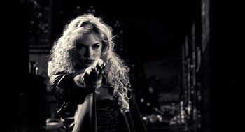 Movie still from “Sin City” (2005), directed by Frank Miller – A woman with long blonde curly hair holding a whip; Medium shot, Over the shoulder angle