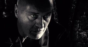 Movie still from “Sin City” (2005), directed by Frank Miller – A black and white photo of a man with green eyes; Extreme Close Up shot, Low angle