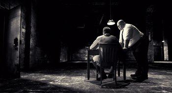 Movie still from “Sin City” (2005), directed by Frank Miller – Two men are sitting at a table in a dark room; Wide shot, High angle