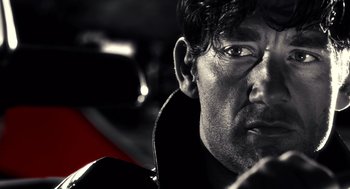 Movie still from “Sin City” (2005), directed by Frank Miller – Black and white photograph of a man in a car; Close Up shot, Low angle
