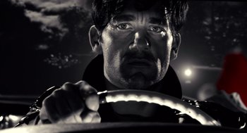 Movie still from “Sin City” (2005), directed by Frank Miller – A black - and - white photo of a man driving a car at night; Close Up shot, Low angle