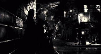 Movie still from “Sin City” (2005), directed by Frank Miller – A black and white photo of a man smoking a cigarette; Medium shot, Low angle