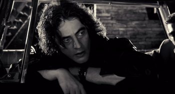 Movie still from “Sin City” (2005), directed by Frank Miller – Black and white photograph of a man leaning against a brick wall; Close Up shot, Low angle