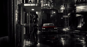 Movie still from “Sin City” (2005), directed by Frank Miller – A woman standing on a street corner in the rain; Wide shot, High angle