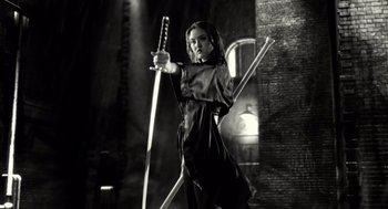 Movie still from “Sin City” (2005), directed by Frank Miller – A woman holding a sword in front of a brick wall; Medium shot, Low angle