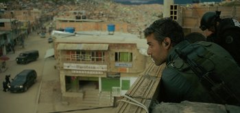 Movie still from “Triple Frontier” (2019), directed by J.C. Chandor – A man wearing a pair of ear buds looking out of a window; Medium shot, Over the shoulder angle
