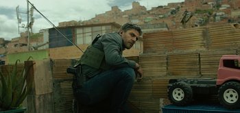 Movie still from “Triple Frontier” (2019), directed by J.C. Chandor – A man with a gun sitting on the ground; Medium shot, Low angle