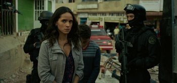 Movie still from “Triple Frontier” (2019), directed by J.C. Chandor – A woman standing next to a man and a man holding a gun; Medium shot, Over the shoulder angle