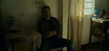 Movie still from “Triple Frontier” (2019), directed by J.C. Chandor – A man sitting on a chair with his arms crossed; Medium shot, Low angle