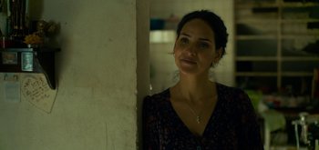 Movie still from “Triple Frontier” (2019), directed by J.C. Chandor – A woman standing next to a wall with a cross on her neck; Close Up shot, Over the shoulder angle