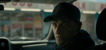 Movie still from “Triple Frontier” (2019), directed by J.C. Chandor – A man in a baseball cap sitting in a car; Close Up shot, Over the shoulder angle