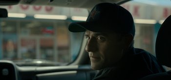 Movie still from “Triple Frontier” (2019), directed by J.C. Chandor – A man wearing a baseball hat sitting in a car; Close Up shot, Over the shoulder angle