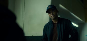 Movie still from “Triple Frontier” (2019), directed by J.C. Chandor – A man wearing a baseball cap and a jacket; Close Up shot, Over the shoulder angle