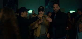 Movie still from “Triple Frontier” (2019), directed by J.C. Chandor – A group of men standing around a woman drinking a beverage; Medium shot, Over the shoulder angle