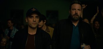 Movie still from “Triple Frontier” (2019), directed by J.C. Chandor – Two men standing next to each other in a dark room; Medium shot, Low angle